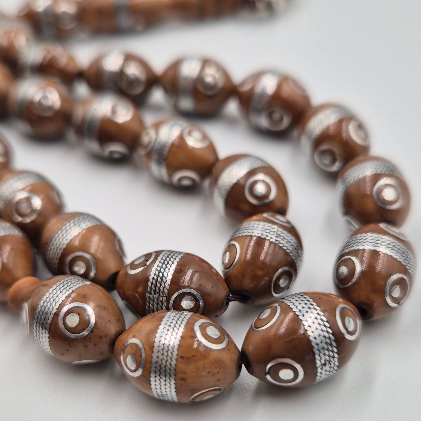 circle of protection and focus. Carved from the resilient Narjil (Coconut) Shell, this tasbih combines organic warmth with metallic precision. Each bead is inlaid with striking Silver-Tone "Orbit" Rings