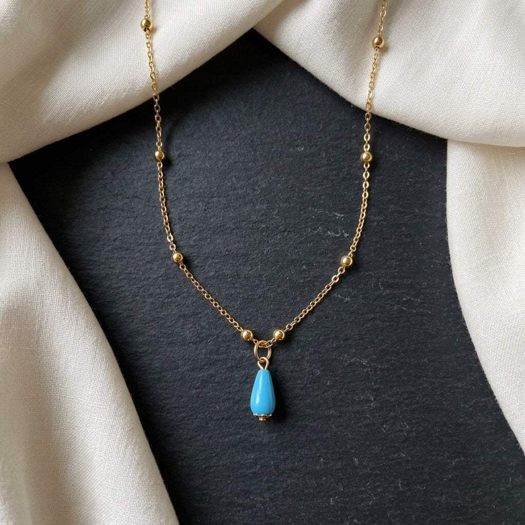 Silver gold-plated Fairouz pendant necklace laid on dark fabric beside cream silk — AtiQ & Jade gemstone jewellery